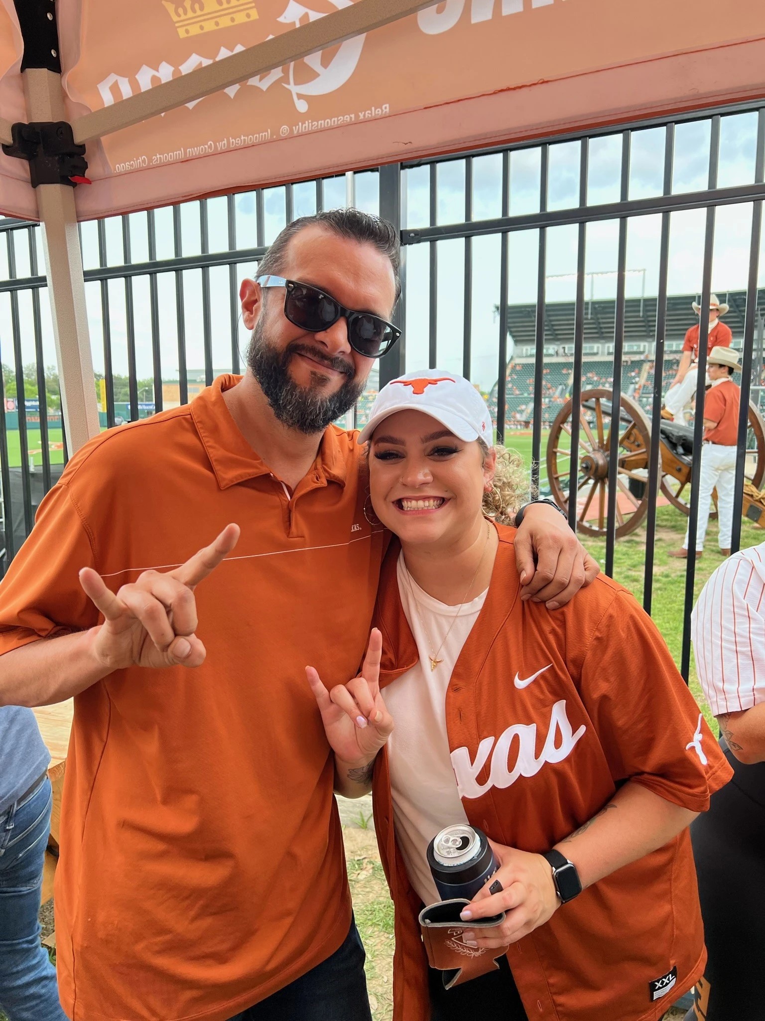 Texas Longhorns fans in orange gear make horns hand gesture at a game.