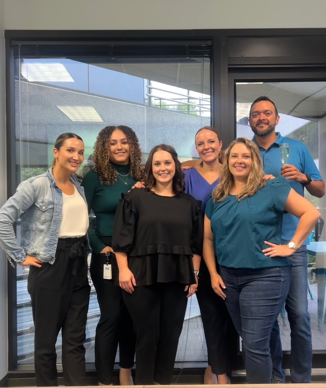 Six people, five women and one man, pose for a photo in an office setting.